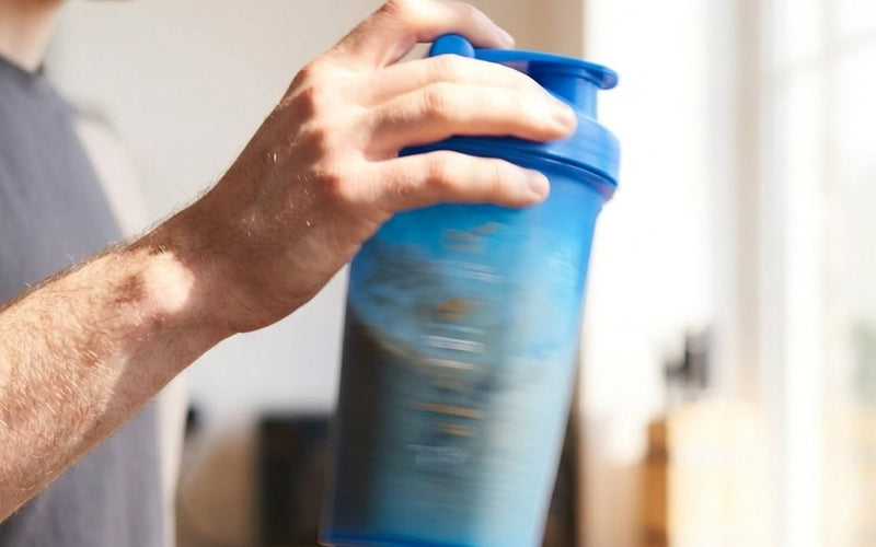 Man shaking a blue shaker bottle in a bright kitchen